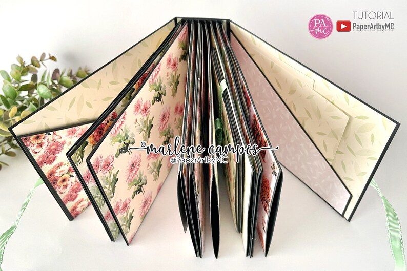 May include: A black and white floral patterned scrapbook with a green ribbon. The scrapbook is open to reveal multiple pages with different floral patterns. The text "marlene campos" and "@PaperArtbyMC" is written on the inside of the scrapbook.