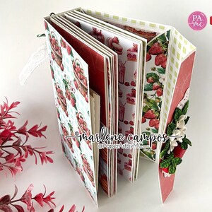 May include: A handmade scrapbook with a strawberry theme. The pages feature strawberry basket and dessert patterns. The cover is decorated with paper flowers and strawberries. The text "marlene campos" and "PaperArtbyMC" are visible.