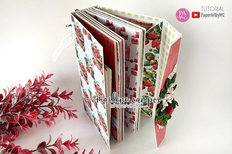 May include: A handmade scrapbook with a strawberry theme. The pages feature strawberry basket and dessert patterns. The cover is decorated with paper flowers and strawberries. The text "marlene campos" and "PaperArtbyMC" are visible.