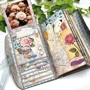 May include: Vintage-style open journal with floral and butterfly illustrations. The pages display roses, butterflies, and decorative elements. The journal is tied with a light blue ribbon.