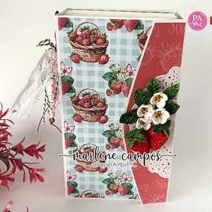 May include: A handmade journal with a strawberry theme. The cover features a basket of strawberries on a light blue gingham pattern. The journal is decorated with paper strawberries, white flowers, and lace. The text "marlene campos" is visible.