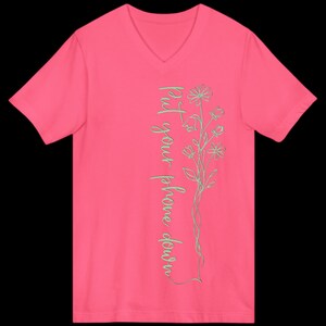Puede incluir: Una camiseta rosa brillante con cuello en V con el texto "Put your phone down" en una fuente cursiva vertical. Un delicado dise&ntilde;o floral en color verde claro acompa&ntilde;a el texto. La camiseta es de color liso y tiene mangas cortas.