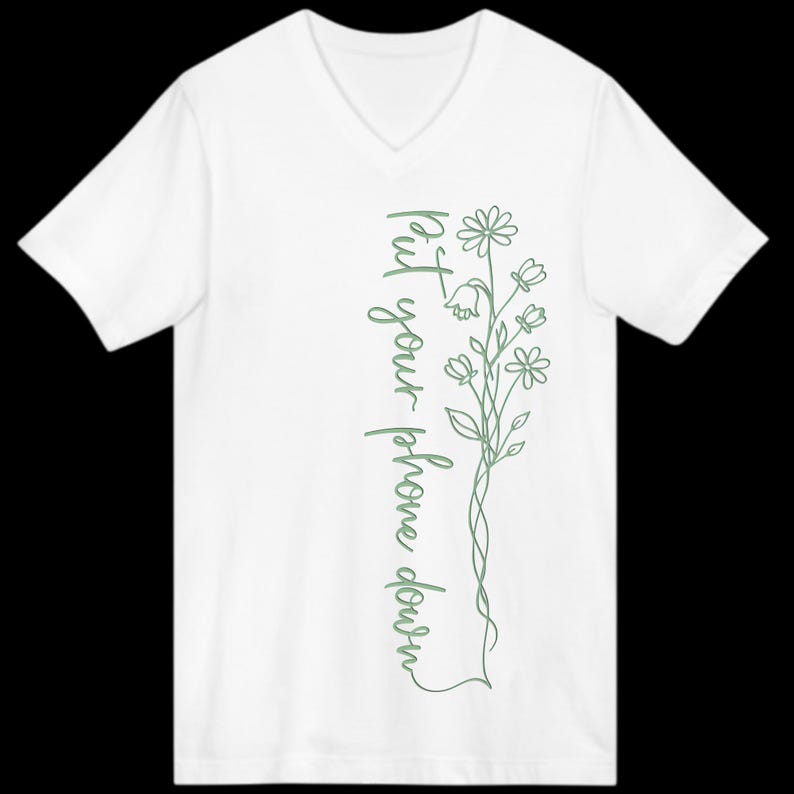 Puede incluir: Camiseta blanca con cuello en V con un dise&ntilde;o floral verde y el texto "put your phone down" en escritura vertical. El dise&ntilde;o presenta flores y hojas delicadas.