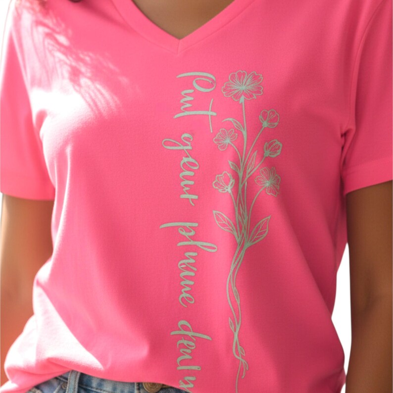 Puede incluir: Camiseta rosa brillante con cuello en V con el texto vertical "Put your prune duty". Un dise&ntilde;o floral verde claro acompa&ntilde;a el texto. La camiseta est&aacute; hecha de un material suave.