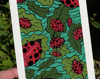May include: A white rectangular card featuring a vibrant illustration of red ladybugs with black spots scattered among green leaves on a teal background. The ladybugs vary in size, creating a dynamic pattern. The card is held against a backdrop of green foliage.