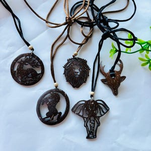 May include: Five brown wooden pendant necklaces with animal designs: a deer, a lion, a horse, an elephant, and a deer head. Each pendant hangs from a cord necklace with an adjustable sliding knot. The necklaces are made of wood.