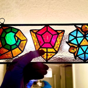May include: A rectangular stained glass panel featuring three distinct geometric shapes. The left shape is a spiral in green and orange, the centre is a pink and orange pentagon, and the right is a blue and orange complex geometric pattern.