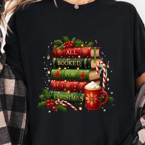 May include: Black t-shirt featuring a stack of books with the words "ALL BOOKED FOR CHRISTMAS." The books are red and green with gold accents, and a candy cane and a mug of hot chocolate are next to the books.