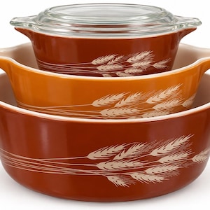 May include: A set of three nested round ceramic baking dishes with integrated handles, featuring a wheat stalk pattern in white against brown and orange exteriors. The smallest top dish includes a clear glass lid with a circular handle.