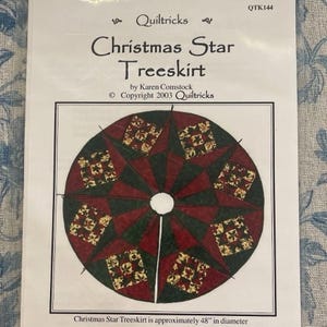 May include: A Quiltricks pattern titled Christmas Star Treeskirt by Karen Comstock, copyright 2003, QTK144. The circular design features a star motif in dark red, dark green, and a cream floral print, measuring 122 cm in diameter.
