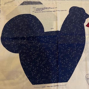 May include: A dark blue fabric pattern piece shaped like a hen, featuring a white vine and leaf print. The piece is labeled BACK and includes printed instructions for embroidery, notions, and a note to leave the bottom open for stuffing.