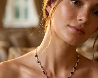 May include: A silver necklace featuring a series of small, teardrop-shaped deep red stones linked together, culminating in a central cluster of five matching teardrop-shaped stones arranged in a fan-like pattern around the neck.
