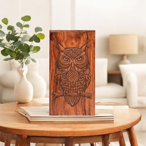 Könnte beinhalten: Rechteckige Holztafel mit einem detaillierten Eulen-Design. Die Eule sitzt auf einem Ast, mit komplizierten Mustern und Texturen. Das Holz hat einen warmen, rötlich-braunen Ton. Die Tafel steht auf einem Tisch.