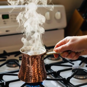 May include: A white ceramic mug with a black handle and the text "But First, Coffee" in a bold, black font. The mug is displayed on a white surface, highlighting its simple design.