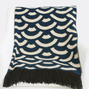 May include: A navy and cream throw blanket featuring a repeating semi-circle design. The blanket has a black fringe along the bottom edge. The throw is draped over a white surface.