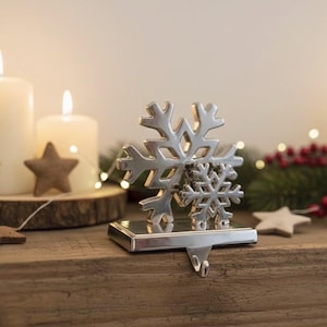May include: A silver snowflake stocking holder on a wooden surface, with lit candles and star-shaped decorations. Festive greenery and lights create a seasonal atmosphere.