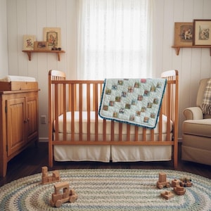 May include: A wooden cot with a blue and white quilt and a white cot skirt. A wooden changing table and shelves with framed pictures are visible. A braided oval rug in blue, green, and white sits on the floor, with wooden toy blocks.