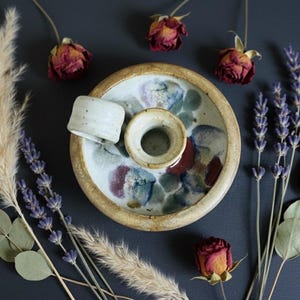 Peut inclure: Un porte-encens en céramique fait à la main, avec un puits central et un petit couvercle assorti. Le support a un bord beige et un intérieur peint avec des accents bleus, verts et rouges. Des roses séchées, de la lavande et des herbes de la pampa entourent le support.