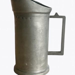 May include: An antique pewter tankard, cylindrical in shape with a rectangular handle. The top rim is angled, and the body has small rivets. This vintage drinking vessel is suitable for display or use. Measures approximately 18 cm in height.