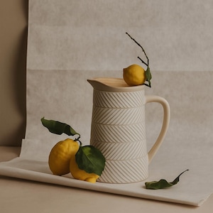 May include: A cream ceramic jug with a wooden lid, featuring a textured chevron pattern. The jug is accompanied by fresh lemons with green leaves. The jug has a handle and is approximately 25 cm tall.