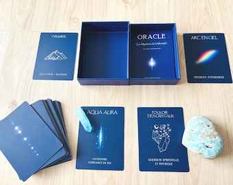 Puede incluir: Una baraja de cartas oráculo azul titulada Oracle Les Mysteres de l'Atlantide con caja, cartas individuales con dibujos y texto en blanco, una punta de cristal azul claro y una piedra mineral azul claro rugosa.