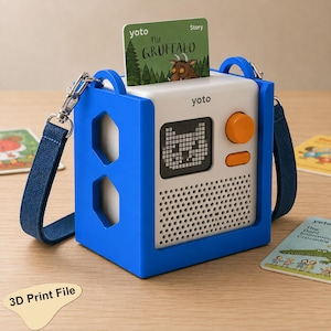 Puede incluir: Un reproductor de audio Yoto blanco dentro de una funda protectora de silicona azul brillante con recortes hexagonales. El dispositivo cuenta con un mando de control naranja, una pantalla pixelada, una rejilla de altavoz y una ranura superior.