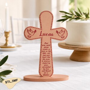 May include: A light brown wooden cross with the name "Lucas" and two dove illustrations. The cross has a stitched border and a base. Text on the cross reads "May! your spirit always remain as pure as the light..."