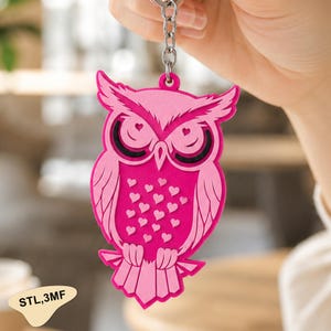 May include: A pink and magenta owl keychain featuring a layered design with heart-shaped pupils and a pattern of small hearts on the chest. The owl has pointed ear tufts and is attached to a silver metal ring. The text STL,3MF is visible.