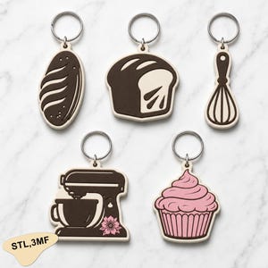 May include: A set of five keychains featuring baking-themed designs: a loaf of bread, a sliced loaf, a whisk, a stand mixer with a pink flower detail, and a cupcake with pink frosting. Each keychain includes a silver metal ring for attachment.
