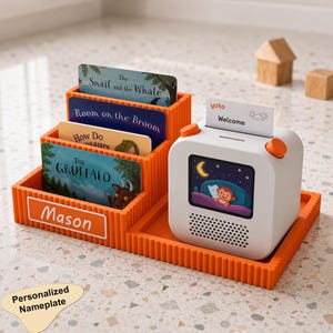 May include: An orange tiered storage organiser with the name Mason printed on the front, holding four children's book cards. Next to it sits a white Yoto audio player with an orange dial and a screen displaying a monkey, with a Welcome card inserted.