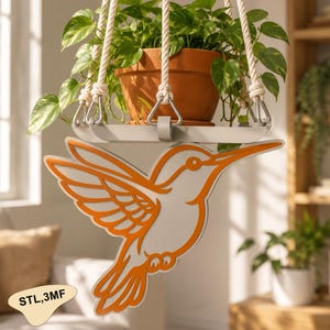 May include: A hanging plant holder featuring a light gray horizontal bar with a cutout orange hummingbird silhouette attached to the front. The holder is suspended by thick white ropes and contains a terracotta pot with a green leafy plant.