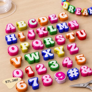 Puede incluir: Una colección de cuentas de plástico coloridas con letras y números, incluyendo el alfabeto de la A a la Z, los números del 0 al 9, un símbolo de almohadilla y un ampersand. Cada cuenta tiene una letra o número blanco sobre un fondo sólido.