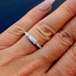 K&ouml;nnte beinhalten: Ein silberner Ring mit einem rechteckigen Mittelteil mit drei kleinen, runden Diamanten. Der Ring hat ein zartes Design mit kleineren, spitzen Akzenten auf beiden Seiten der Mitte.