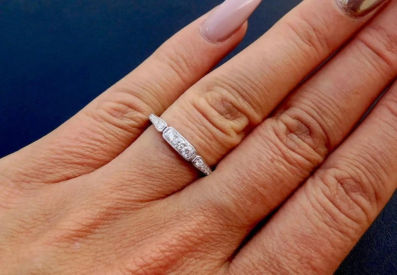 K&ouml;nnte beinhalten: Ein silberner Ring mit einem rechteckigen Mittelteil mit drei kleinen, runden Diamanten. Der Ring hat ein zartes Design mit kleineren, spitzen Akzenten auf beiden Seiten der Mitte.