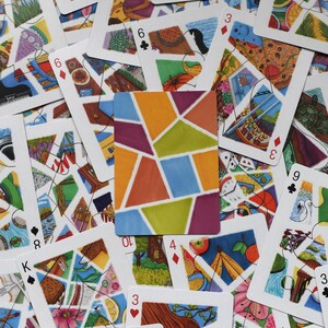 Può includere: Un insieme di carte da gioco con disegni astratti e colorati. Una carta presenta un motivo geometrico arancione, viola, verde e blu. Altre carte mostrano varie illustrazioni, inclusi numeri e semi. Le carte sono sparse.