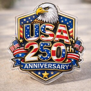 Puede incluir: Un emblema conmemorativo con el texto "USA 250th Anniversary". El diseño presenta un águila calva, banderas americanas y estrellas. El emblema es de color rojo, blanco, azul y dorado.