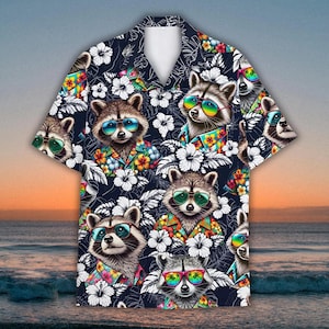 May include: A short-sleeved, button-down shirt with a dark blue background. The shirt features a repeating pattern of raccoons wearing sunglasses and Hawaiian shirts, interspersed with white hibiscus flowers. The shirt is a vibrant and colorful design.
