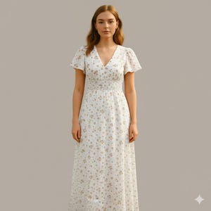 Könnte beinhalten: Ein weißes Maxikleid mit floralem Muster, V-Ausschnitt und kurzen Fledermausärmeln. Das Kleid hat ein eng anliegendes Oberteil mit gerüschter Taille und einen fließenden Rock. Das Blumenmuster ist in gedämpftem Gold gehalten.