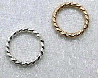 May include: Two twisted metal rings, one silver and one gold, on a white textured background.