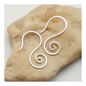 May include: A pair of silver-colored, spiral-shaped earrings. The earrings have a hook design for easy wear. The spiral design adds a unique and elegant touch to the jewelry. The earrings are displayed on a light brown, textured surface.