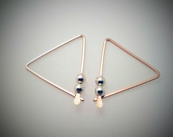 May include: A pair of triangle-shaped earrings with two silver beads on each earring. The earrings are made of rose gold metal.