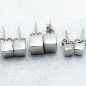 May include: Three pairs of silver cube stud earrings. The earrings are in three different sizes.