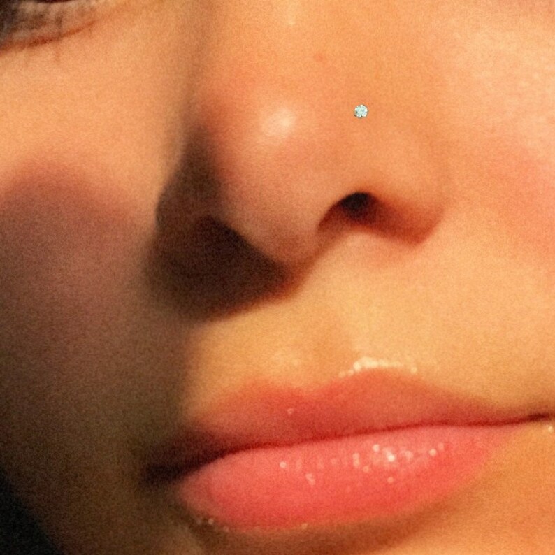 May include: Close-up of a person's face with a small, clear nose ring.
