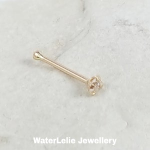 May include: A gold nose ring with a small clear gemstone. The ring is straight and has a rounded end.