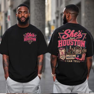 May include: A black t-shirt featuring a graphic design with the text "She's from HOUSTON I CAN TELL". The front has a small logo, while the back displays a large illustration of the Houston skyline, an astronaut, a cowboy boot, and a drink cup.