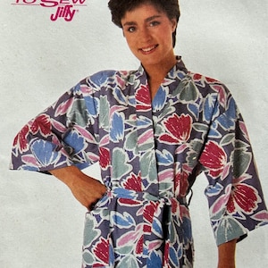 May include: Simplicity sewing pattern featuring a woman in a floral print robe. The pattern cover has the text "E-A-S-Y TO SEW Jiffy" and "Simplicity" in large pink letters. The robe is blue with red and blue floral designs.