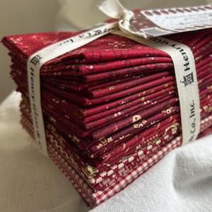 May include: A stack of red fabric squares, tied with a cream-colored ribbon that reads "Henry Glass & Co., Inc." A small tag is attached to the ribbon. The fabric has various patterns, including floral and gingham.