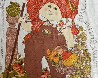 Op de afbeelding: Een vintage Cabbage Patch Kids stoffen paneel met een pop met rood haar, een bruine overall en een schop. Een mand met producten en een kikker op een voetstuk zijn ook afgebeeld. De tekst "LEAVE OPEN FOR STUFFING" staat onderaan.