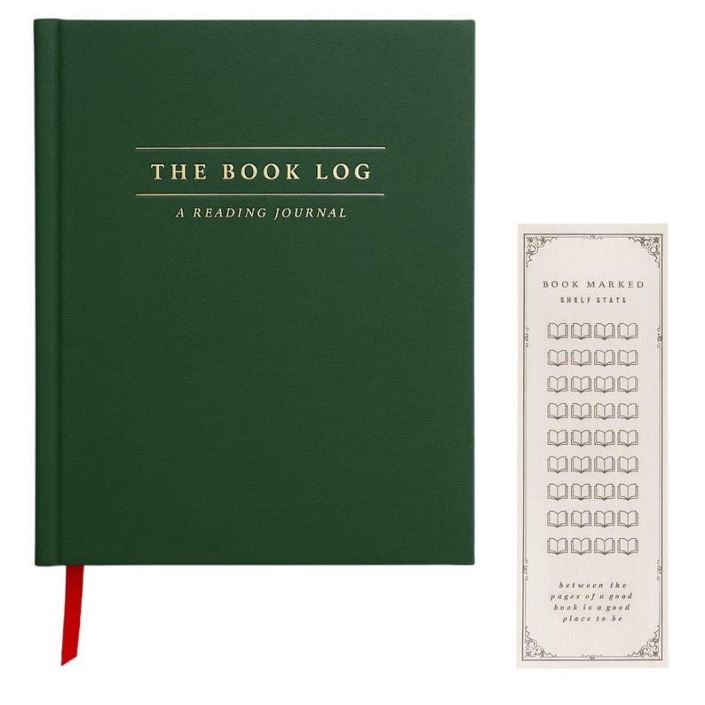May include: A dark green hardcover reading journal with the gold text THE BOOK LOG A READING JOURNAL on the front cover and a red ribbon bookmark. Beside it is a tall, narrow cream-colored bookmark with the text BOOK MARKED SHELF STATS.