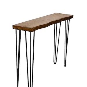 May include: A rustic console table with a natural wood top and black hairpin legs. The table's top has a live edge, showcasing the wood's natural shape. The legs are made of black metal and are angled for stability.
